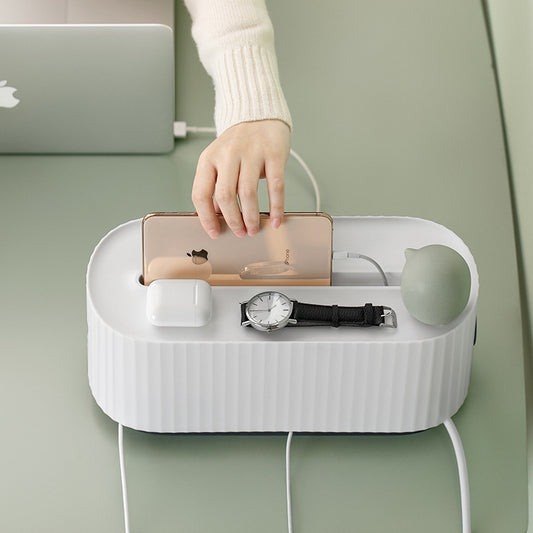  The Cloud Power Storage Box in white is displayed on a green table, with a person placing a beige phone on top. It showcases the box's spacious top, ideal for holding phones and small items, and emphasizes its role as a cable organizer.