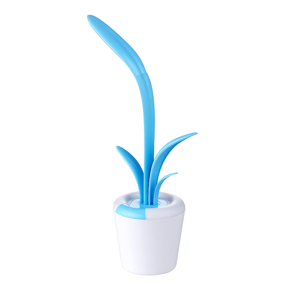 mage displays a blue green Clivia LED Table Lamp. The lamp, resembling a stylized plant, has a white, pot-like base and two green, leaf-shaped elements that extend upward. 