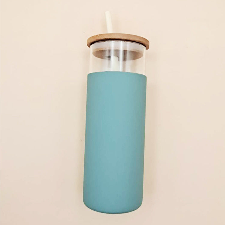 glass cups standing upright in a row, in pastel shades of teal, navy, and pink, each with a wooden lid and a matching glass straw placed on a beige background.