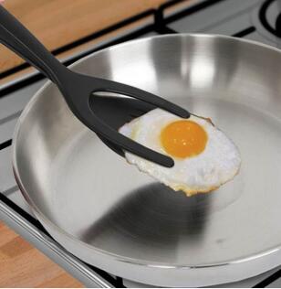 2 In 1 Grip And Flip Tongs lifting a fried egg from a stainless steel pan. The tongs' flexible and food-grade silicone material ensures easy flipping and gripping without damage.
