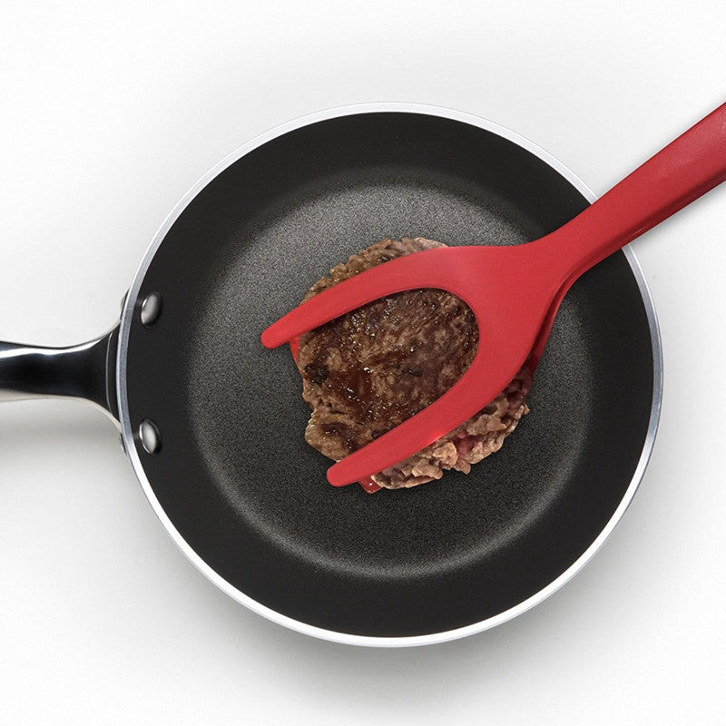 2 In 1 Grip And Flip Tongs being used to flip a hamburger patty in a frying pan. The tongs' heat-resistant and non-stick material makes cooking meat easy and safe