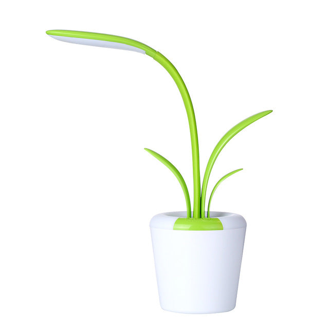 mage displays a single green Clivia LED Table Lamp. The lamp, resembling a stylized plant, has a white, pot-like base and two green, leaf-shaped elements that extend upward. 