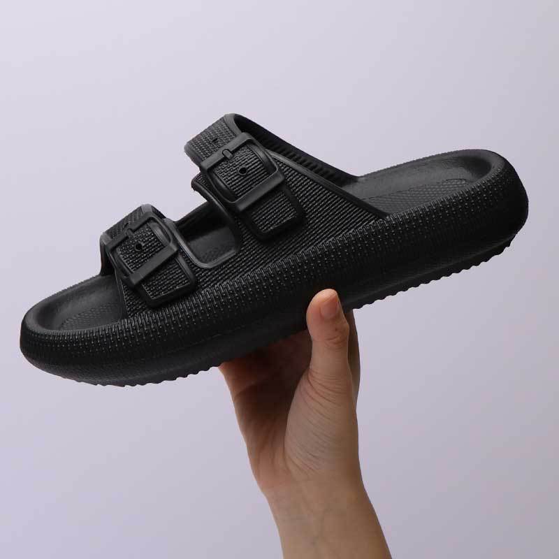  a black-colored platform slipper with a buckle, against a creamy beige background.