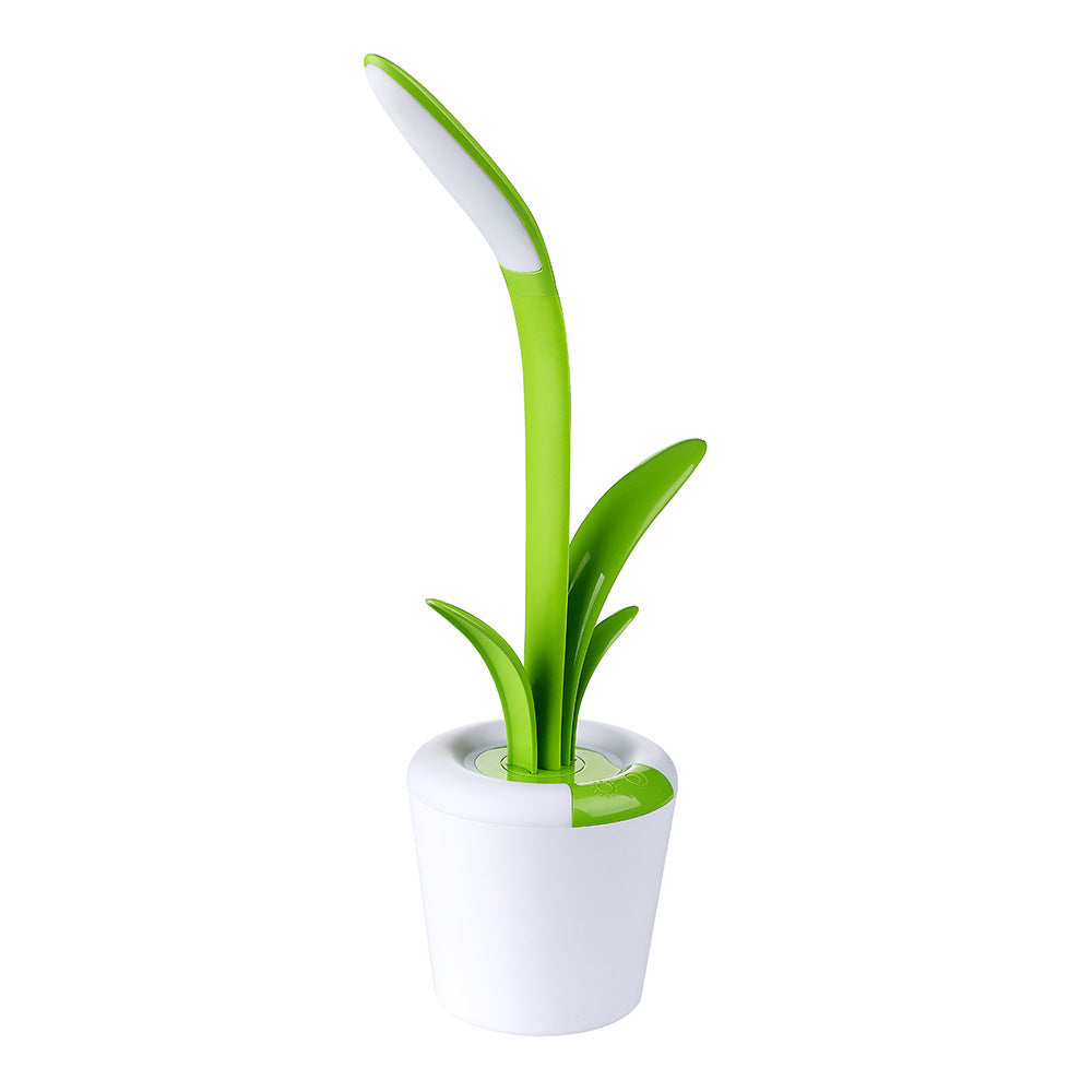 mage displays a single green Clivia LED Table Lamp. The lamp, resembling a stylized plant, has a white, pot-like base and two green, leaf-shaped elements that extend upward. 