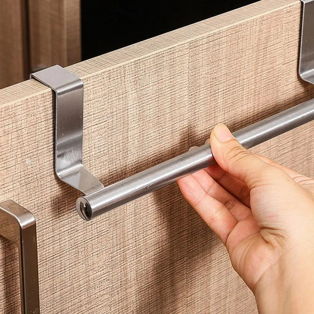 A hand is holding a cylindrical stainless steel towel bar attached to a textured wooden cabinet door via two metallic brackets.