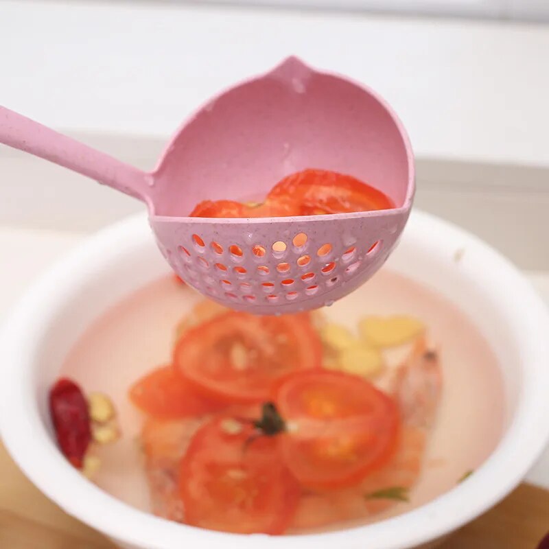 Close-up of the ladle, now in pink, scooping tomato slices from a bowl of water, highlighting the strainer feature and the round wide spoon surface.