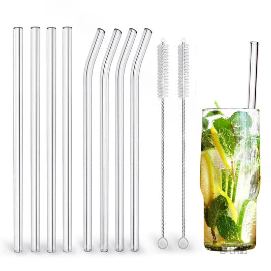 This image displays a set of transparent borosilicate glass drinking straws, some straight and some bent, alongside two cleaning brushes with looped ends for easy handling. On the right side, there's a glass containing a refreshing drink with mint leaves, showcasing one of the straws in use