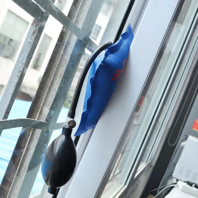 a blue Super PDR Pump Wedge placed vertically between a window frame and sash, demonstrating its use in adjusting and aligning windows during repairs or installation.
