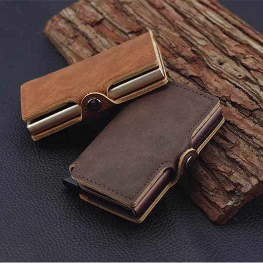 The image displays two RFID aluminum card holders, one in dark brown and the other in a lighter tan color, both with a leather finish. They have a metallic mechanism on the side and are designed to hold cards securely. They are placed atop a wooden log, showcasing their compact and stylish design.