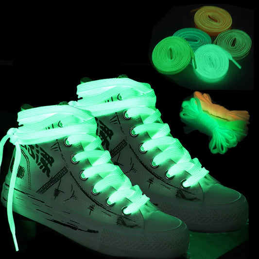 The image shows a pair of sneakers with glow-in-the-dark shoe laces. The laces glow a bright neon green in the dark, contrasting against the darker background. Above the sneakers, there are three separate coiled laces also glowing, hinting at the variety of colors available for these laces.