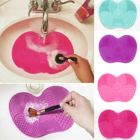 A hand is cleaning a black makeup brush on a heart-shaped pink silicone pad in a white sink, with water running from the tap, demonstrating the usage of the Silicone Makeup Brush Cleaner Pad.