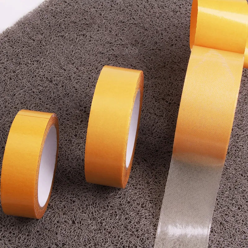 Three rolls of varying widths of double-sided mesh tape displayed on a gray surface.