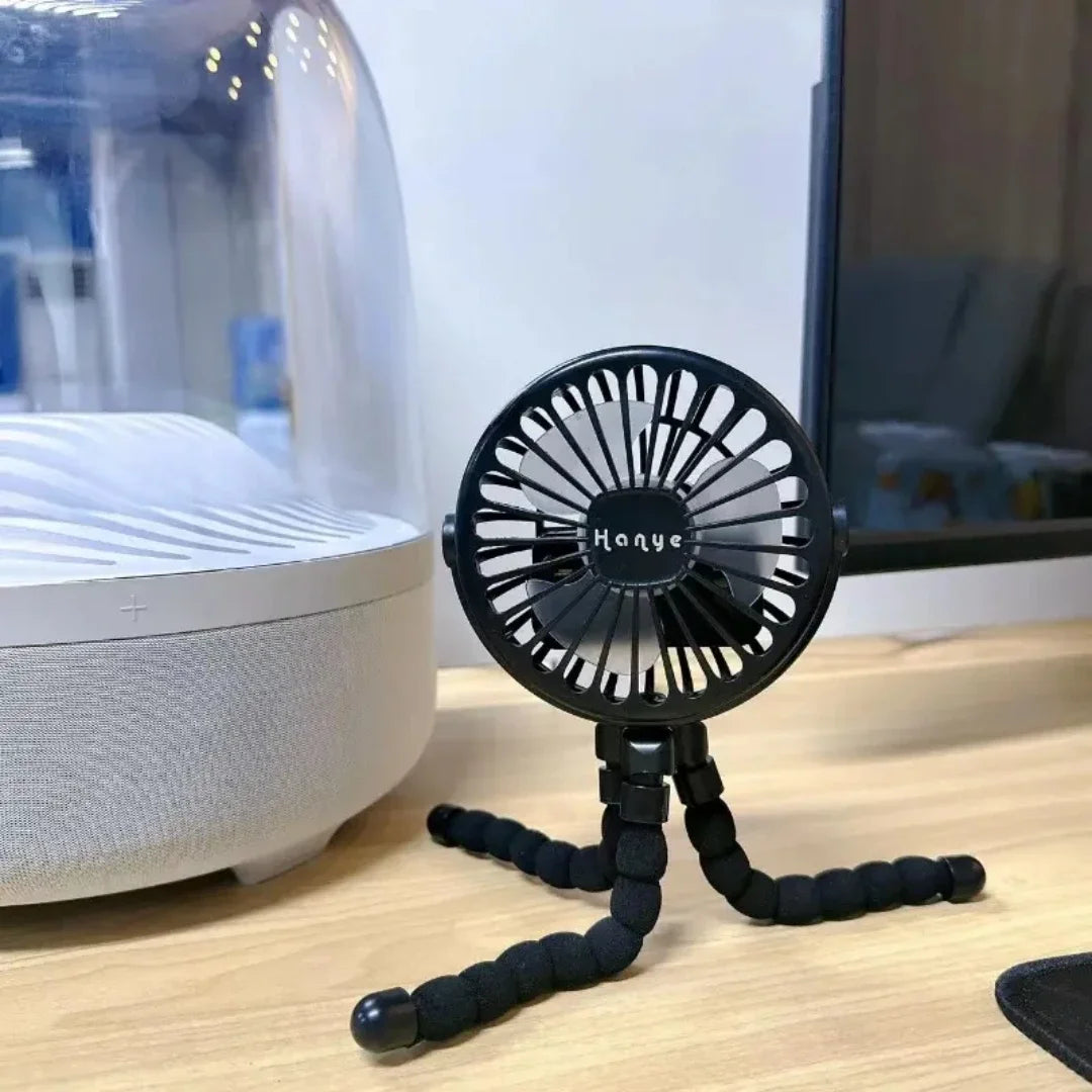 A black USB rechargeable fan on a table with its flexible tripod legs positioned for stability and convenience.