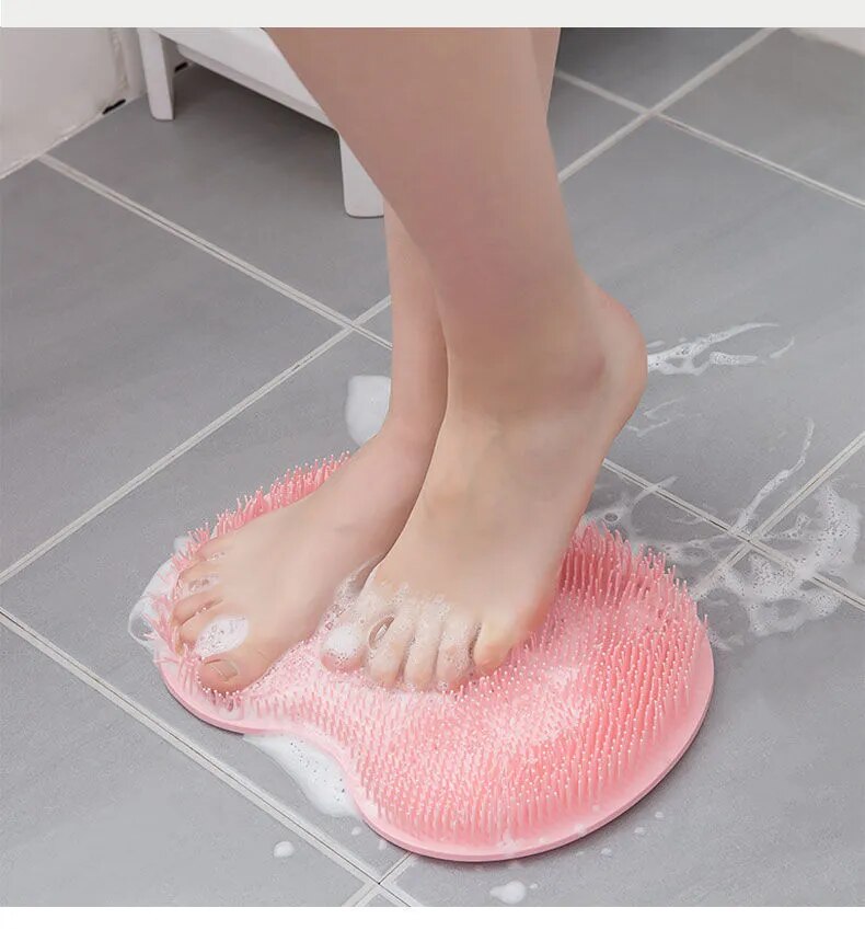A close-up of a foot pressing down on a pink silicone scrubber on the floor, illustrating its use for cleaning feet.