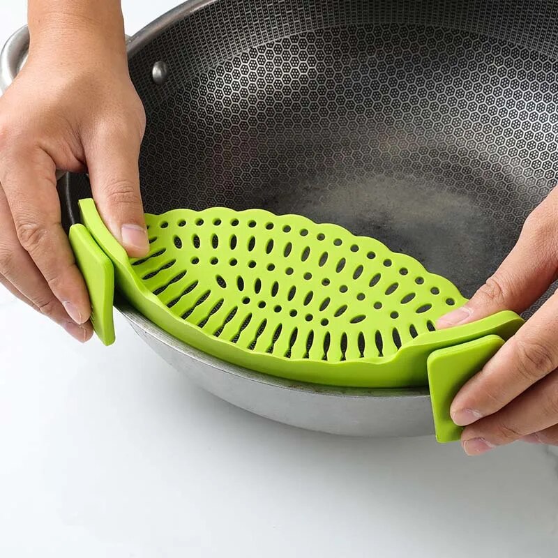 A close-up of a green silicone strainer attached to a pot, focusing on its round and oval draining holes