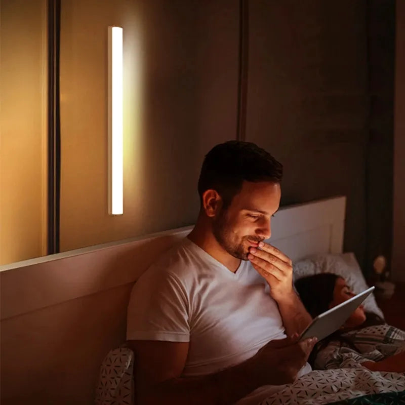 A person is reading in bed with the light affixed above, suggesting the light's use as a personal reading lamp that can be mounted to different surfaces.