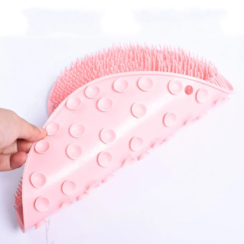 A person is adhering a pink, kidney-shaped silicone scrubber to a tiled wall, showcasing the suction capability.