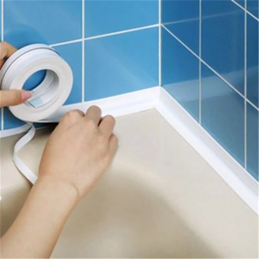 A person is applying a white sealing strip to the joint between a beige bathtub and blue tiled wall, smoothing it down with their fingers.