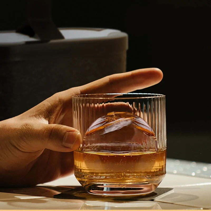 Ice Ball and Whiskey: A hand holding a whiskey glass with a large, clear ice ball inside, showcasing the ice ball maker’s ability to create perfect ice spheres for beverages.