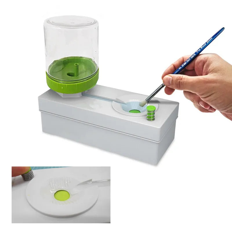 A cylindrical transparent brush washing bucket with a green lid, shown with a blue paintbrush being inserted.
