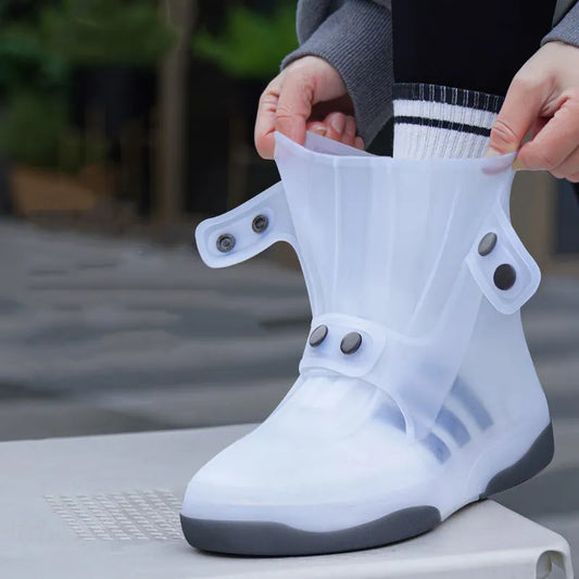 The image shows a person standing on a textured surface, fitting a translucent white shoe cover over their footwear. The cover has a high-top design with two black snap buttons on the side, creating a secure fit around the ankle. The material appears waterproof and durable, designed to protect shoes from water and dirt.