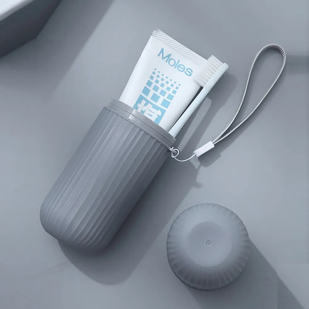 An open grey toothbrush cup with a toothbrush and toothpaste inside, alongside a closed cup, presented on a white surface.