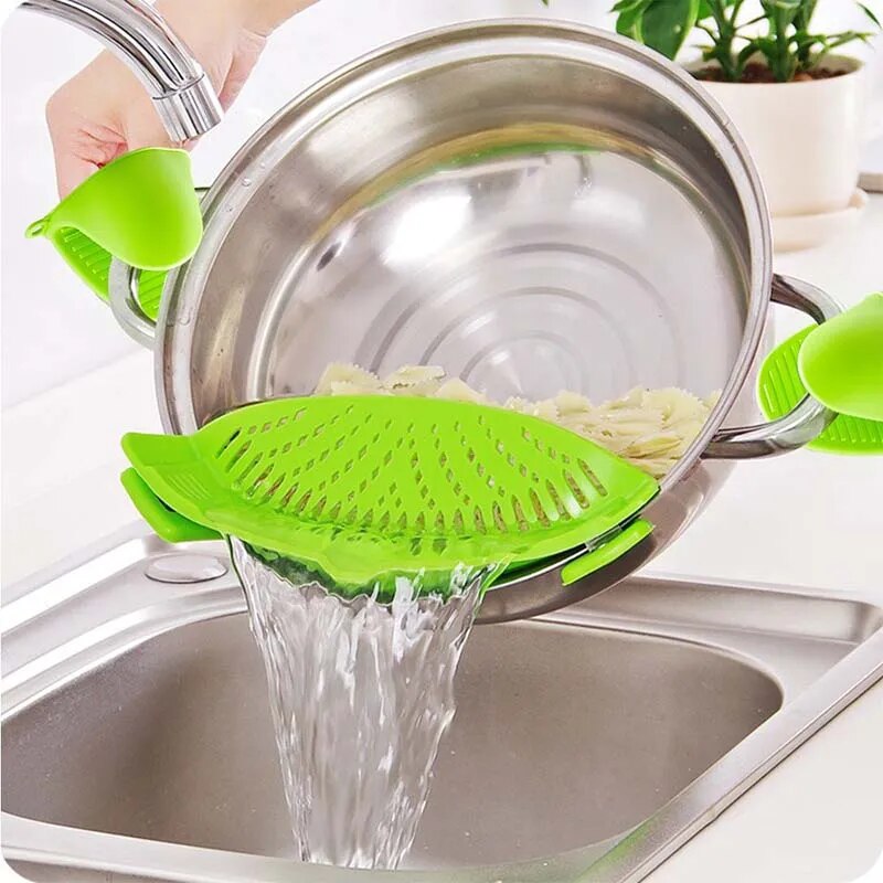 A green silicone strainer is clipped onto a pot of pasta, demonstrating its use for draining water from foods.