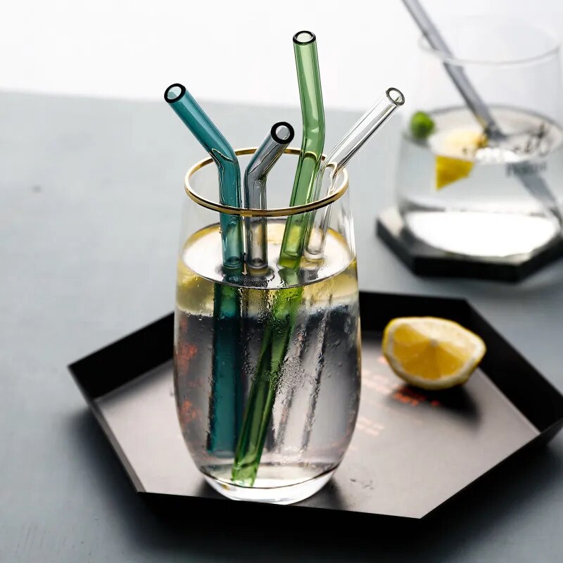 A glass filled with ice water, containing a clear glass straw, alongside a lemon slice, set on a black napkin with a sleek dining setup