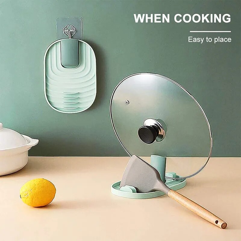 The image displays a mint green silicone pot lid holder mounted on a wall, with grooved design for resting kitchen utensils. A clear pot lid with a black knob is placed on a countertop next to the holder, which also supports a grey spatula with a wooden handle.