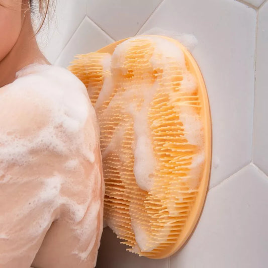 An individual uses a large yellow silicone back scrubber on their back, covered in soapy lather.