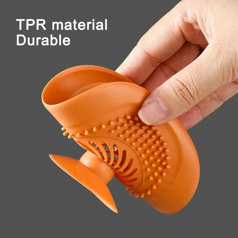 A person’s hand is squeezing an orange silicone sink strainer, demonstrating its flexibility and the holes that catch debris.