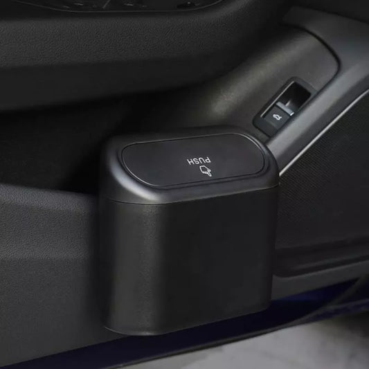 A compact, black car trash bin installed on a vehicle's lower door panel, looking sturdy and seamlessly integrated with the car's interior.