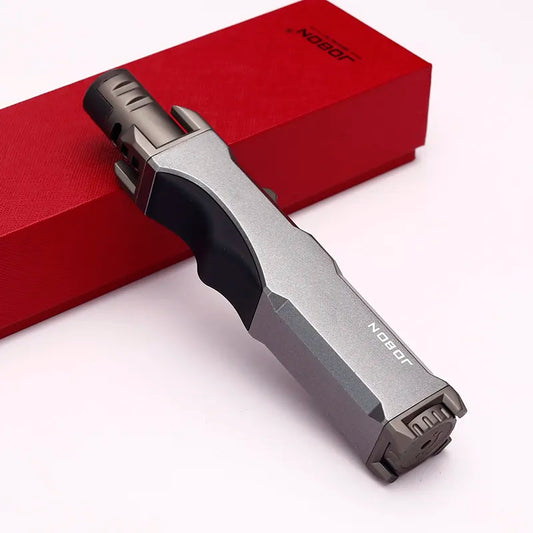 The windproof turbine torch lighter, presented in a sleek black design, is showcased with its red box. This high-quality butane torch is ideal for various outdoor and kitchen uses
