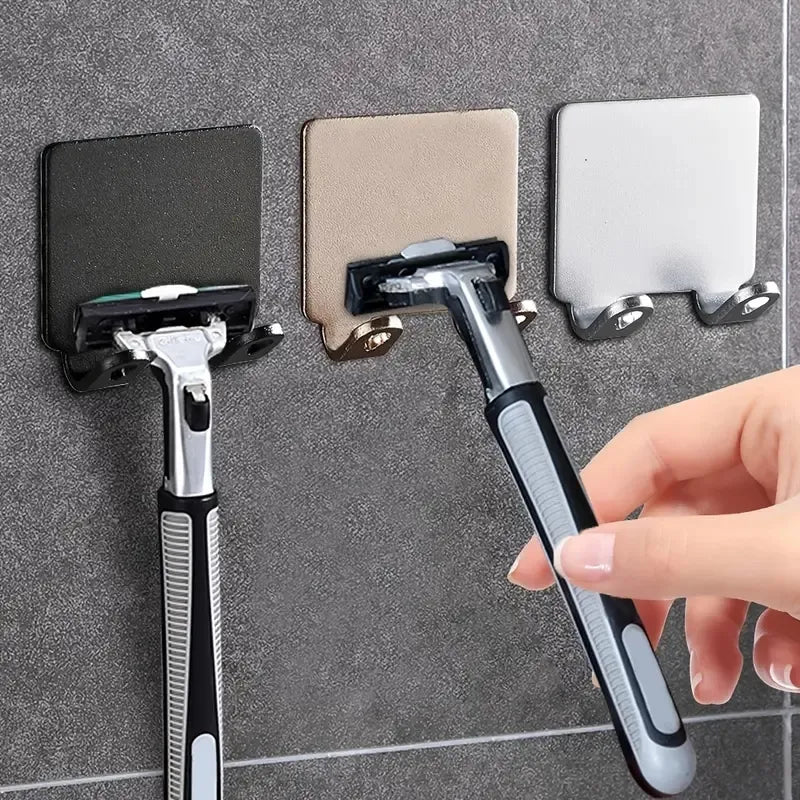 The image shows two square, wall-mounted razor holders, one in silver and the other in black, designed to hold razors securely in place. Both holders feature a central slot for inserting a razor handle, ensuring easy access and storage in a bathroom setting.