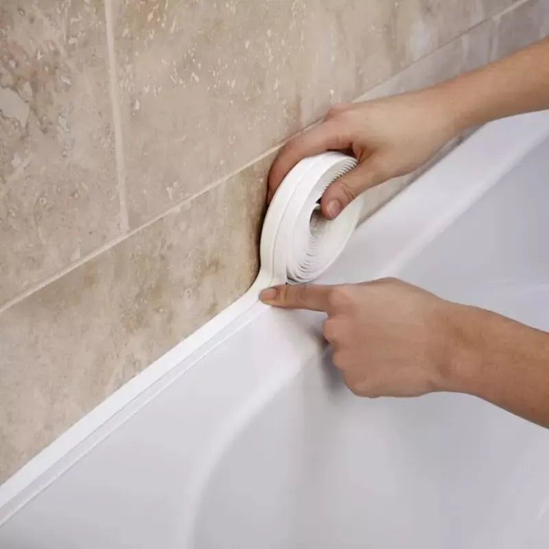 An individual is pressing a white, self-adhesive sealing strip into the corner where a beige bathtub meets beige-tiled walls.