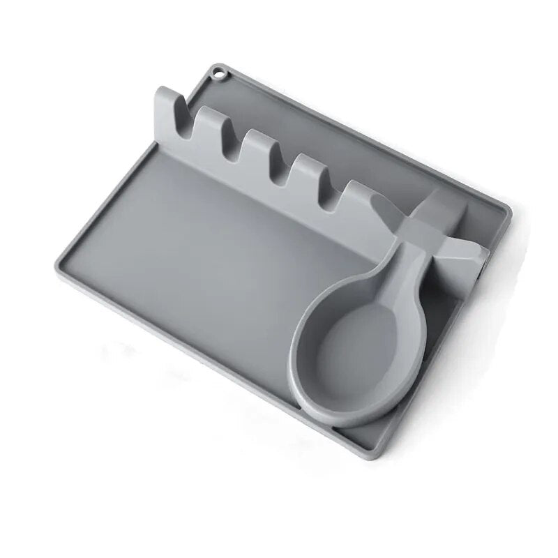 Image depicts a close-up of a grey silicone spoon rest with a dedicated slot for a spoon and a raised edge to prevent drips on the surface.