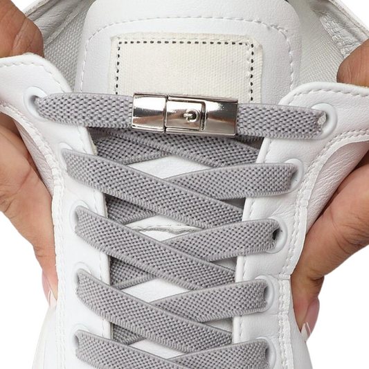 The image displays a close-up view of a shoe with gray, no-tie shoelaces threaded through white eyelets. The laces are secured with a high-quality metal buckle mechanism, showcasing a sleek and practical design that eliminates the need for tying knots.