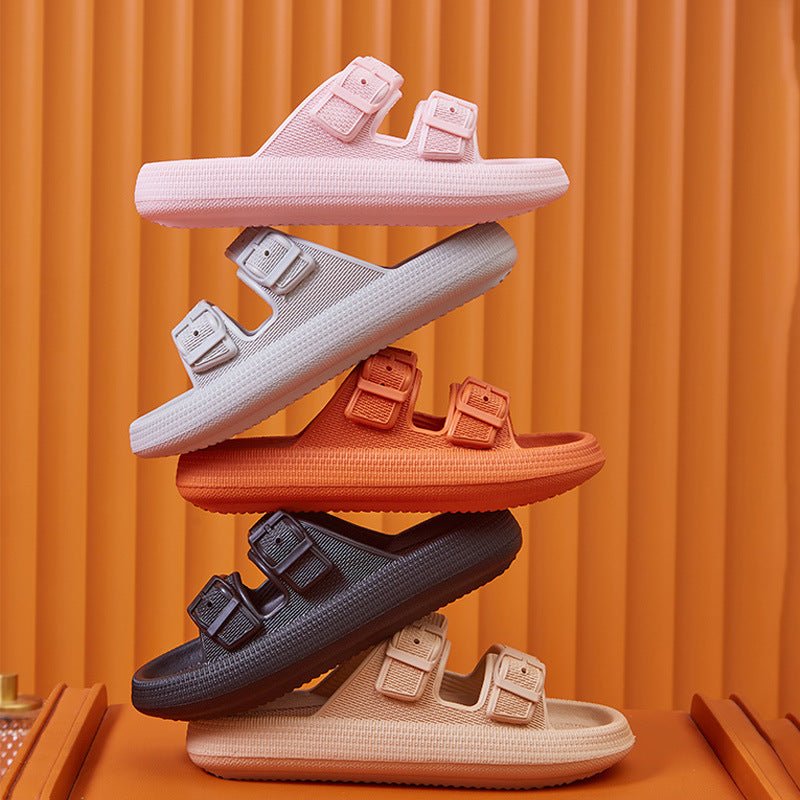 A collection of platform slippers in various colors (black, white, pink, and grey) is displayed with one slipper propped up on a small orange platform.