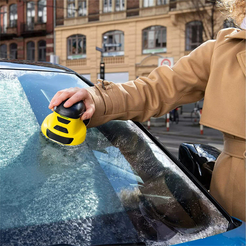 A handheld, cordless electric snow scraper in action, with its yellow and black casing, is shown removing snow from a car's windshield against a wintry backdrop.