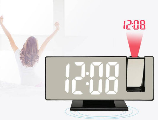 A digital alarm clock displays the time "12:08" in large white numbers on a black background, with a projection of the time on a wall above a bed where a person is stretching.