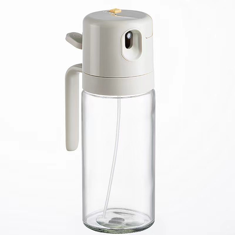 The image showcases a sleek 2-in-1 Oil Sprayer Bottle made of transparent glass, featuring a modern, warm gray top with a built-in handle for easy grip. It’s designed for convenient one-hand operation in the kitchen.